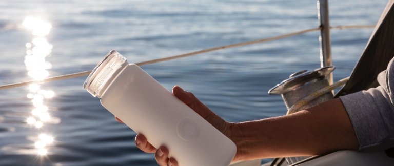 A reusable water bottle. Background is showing the ocean.